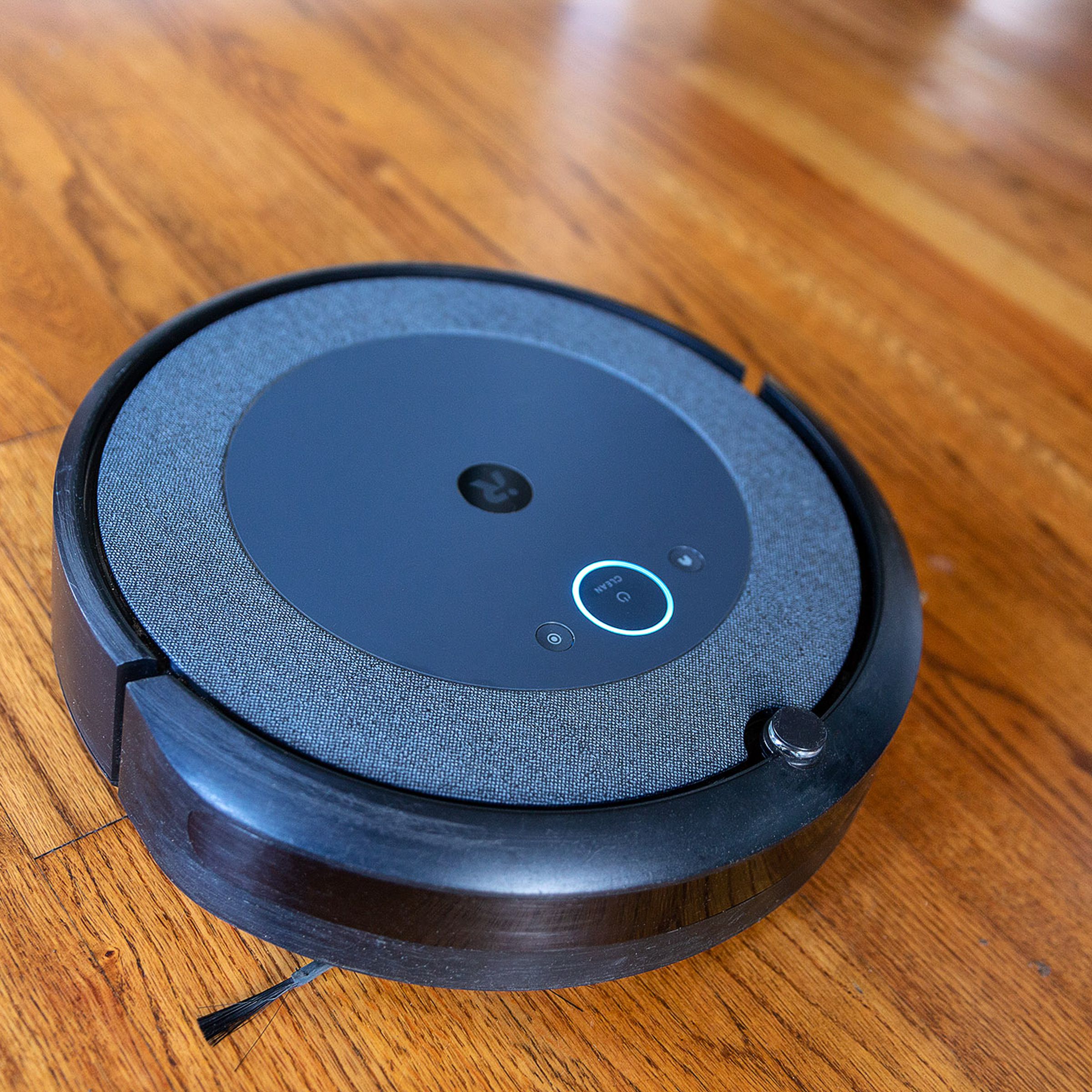 The iRobot Roomba i3 Plus EVO robot vacuum cleaner lies on a wooden floor.