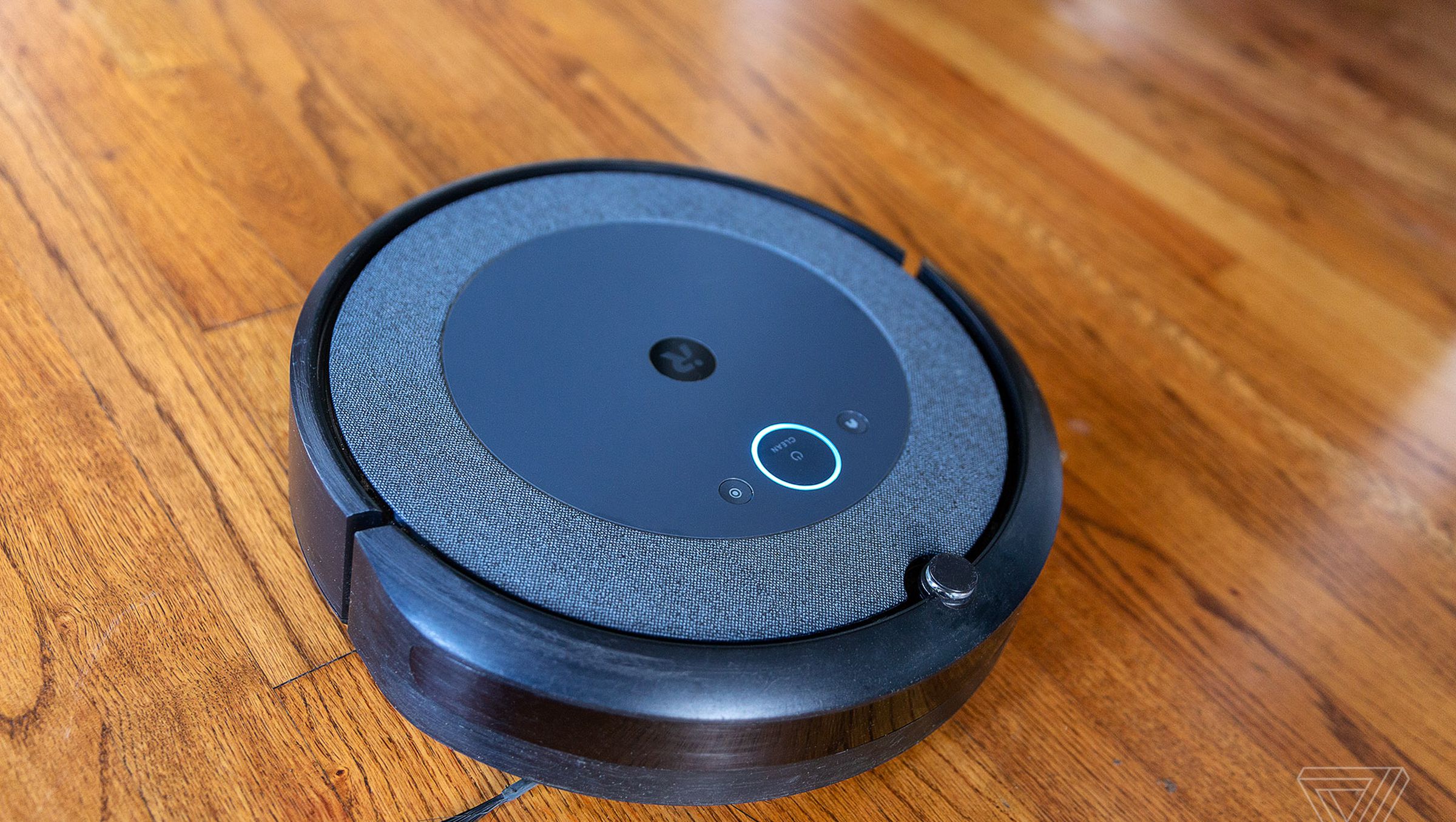 The iRobot Roomba i3 Plus EVO robot vacuum cleaner lies on a wooden floor.